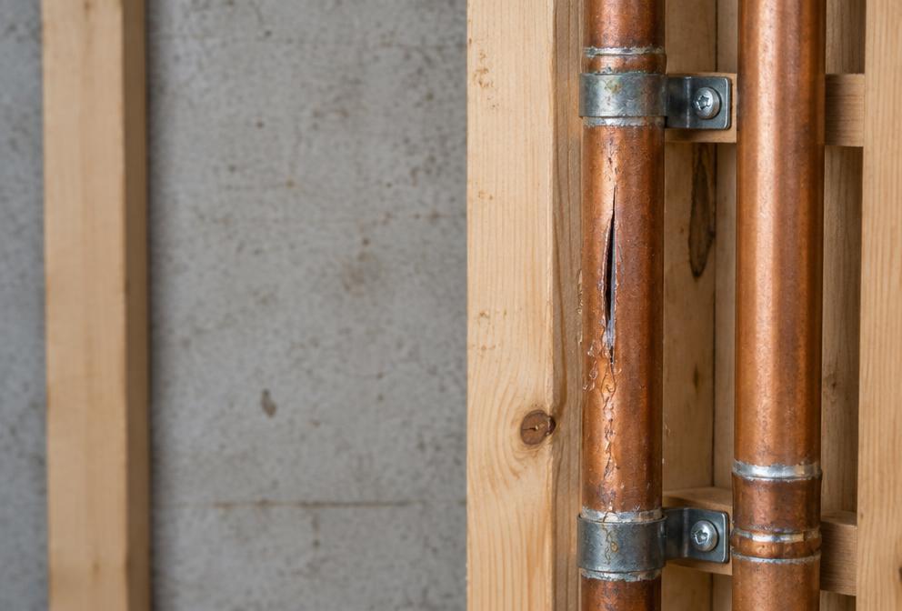 Visible split in an exposed copper water supply pipe beside adjacent intact piping